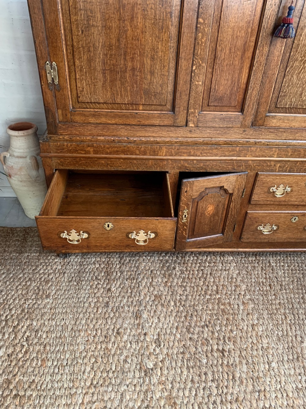 A late Georgian oak press cupboard featuring fielded panel doors with inlay motifs, H-hinges, and a base fitted with drawers and brass hardware. View XIII