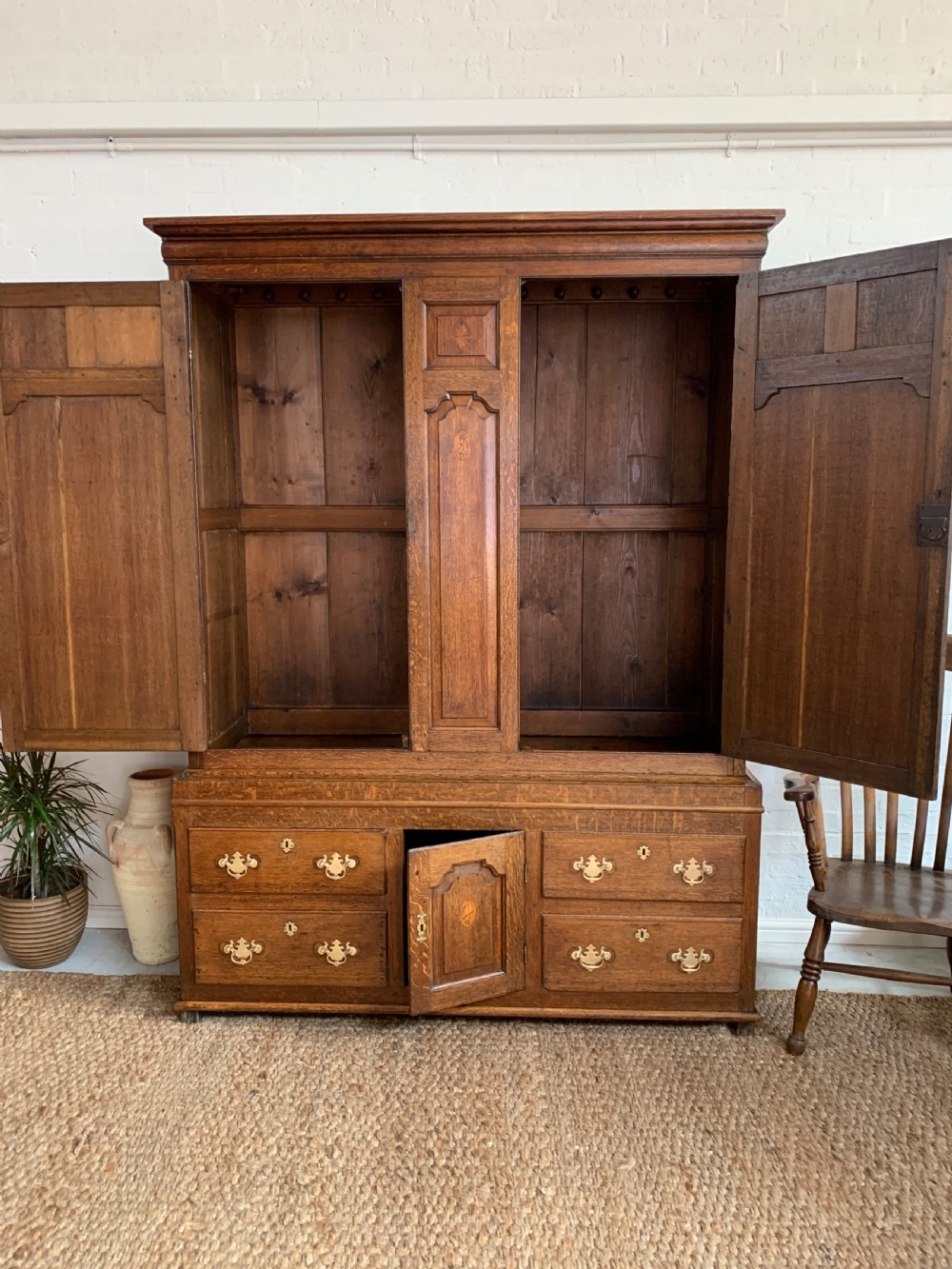 A late Georgian oak press cupboard featuring fielded panel doors with inlay motifs, H-hinges, and a base fitted with drawers and brass hardware. View XIV
