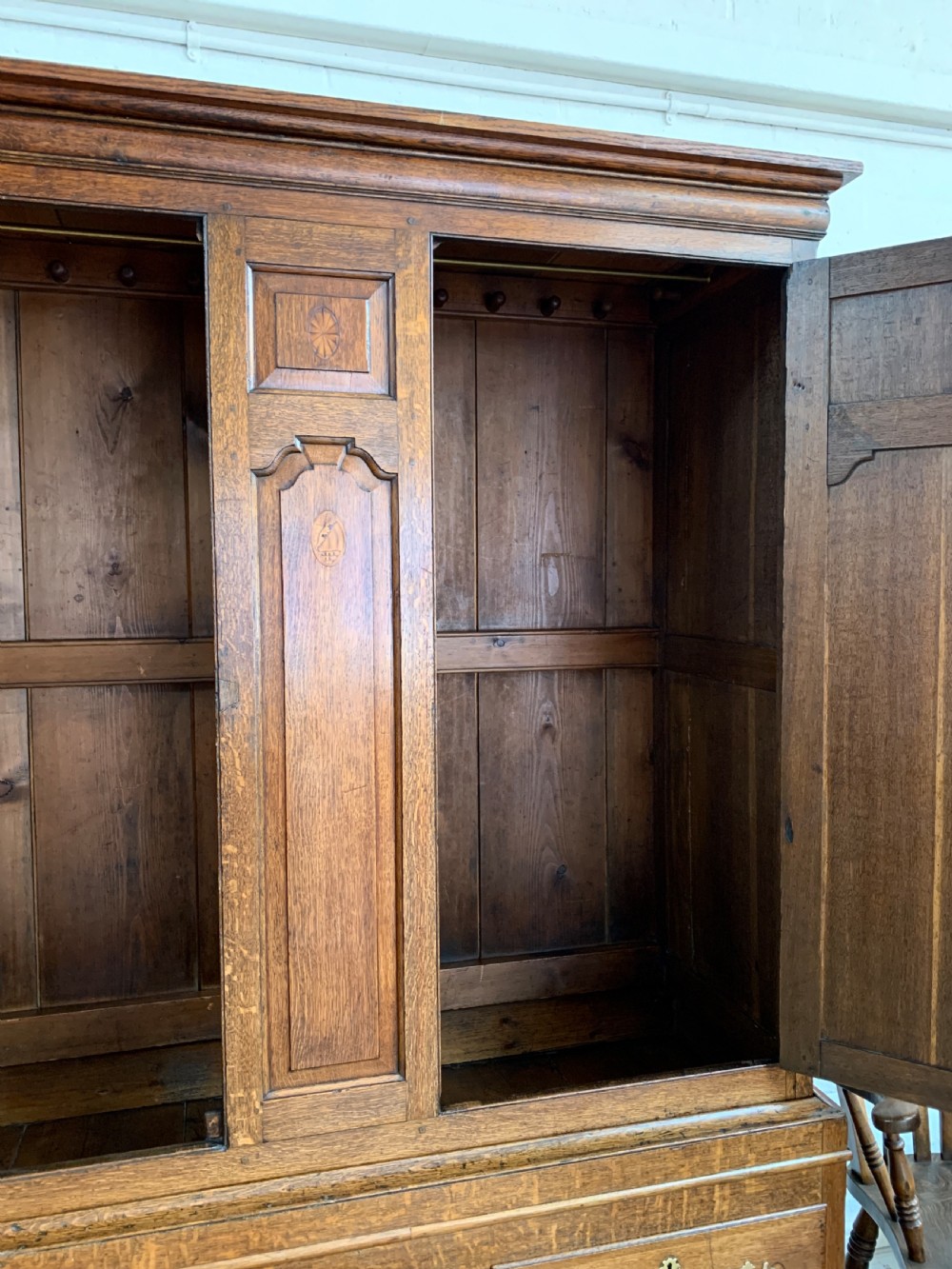 A late Georgian oak press cupboard featuring fielded panel doors with inlay motifs, H-hinges, and a base fitted with drawers and brass hardware. View XV