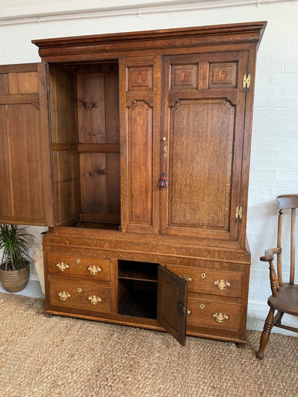 A late Georgian oak press cupboard featuring fielded panel doors with inlay motifs, H-hinges, and a base fitted with drawers and brass hardware. View XVI