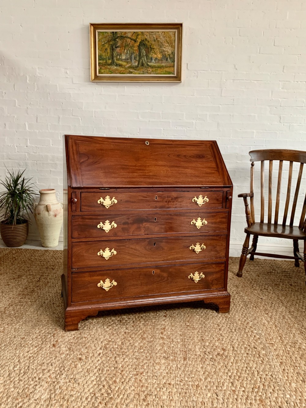 A Georgian mahogany slant-front writing bureau featuring four graduated drawers with brass batwing handles and bracket feet.