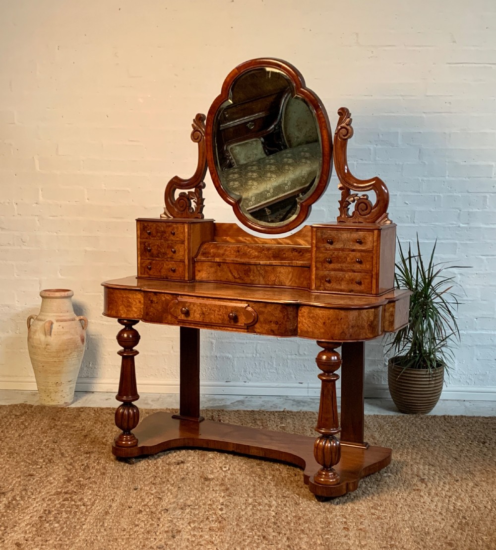 A Victorian burr walnut dressing table featuring a central oval mirror with carved supports, raised trinket drawers, and turned front legs on a plinth base.