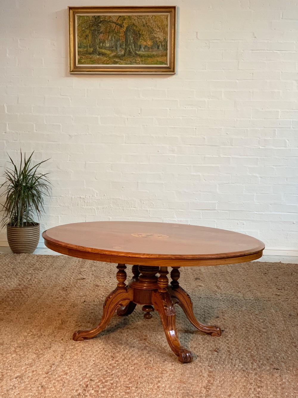 An oval Victorian walnut coffee table featuring central floral marquetry inlay on top and a hand-carved quadruped pedestal base.