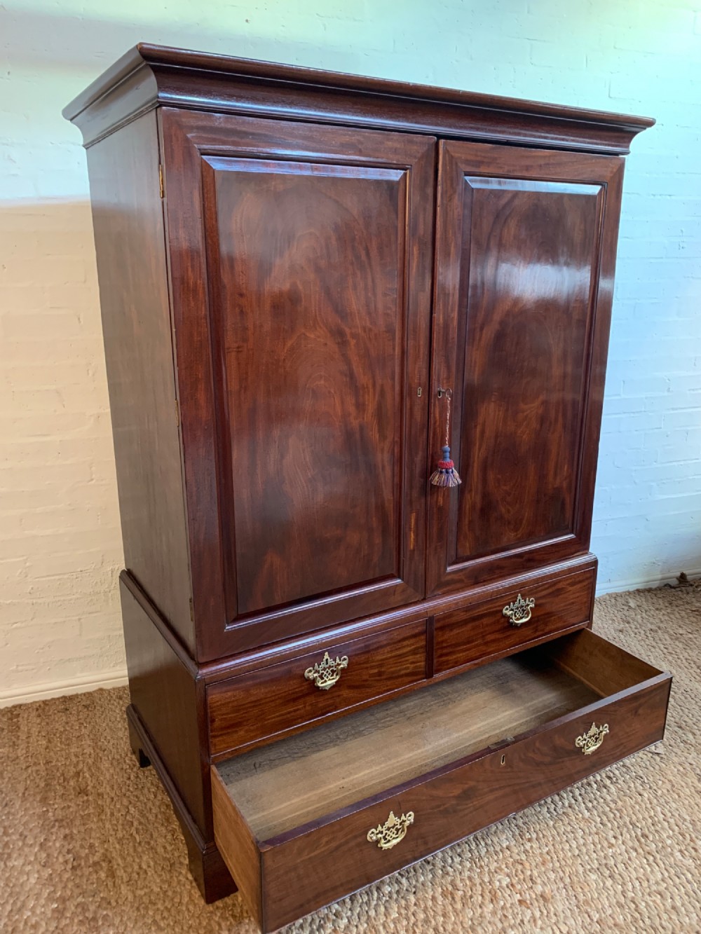 A 19th-century mahogany linen press featuring a two-door upper cupboard above a base with drawers and brass handles. View IV