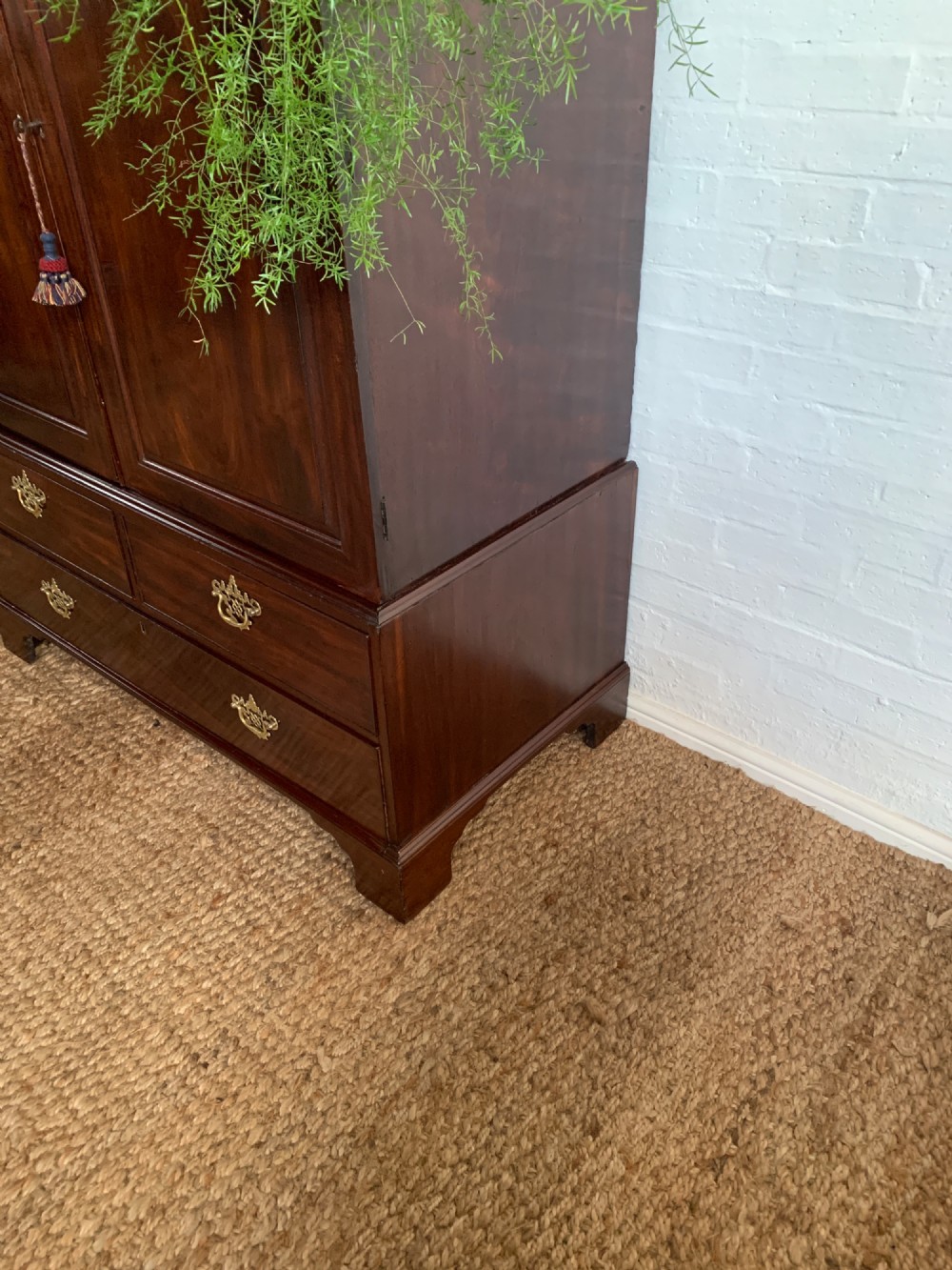 A 19th-century mahogany linen press featuring a two-door upper cupboard above a base with drawers and brass handles. View V