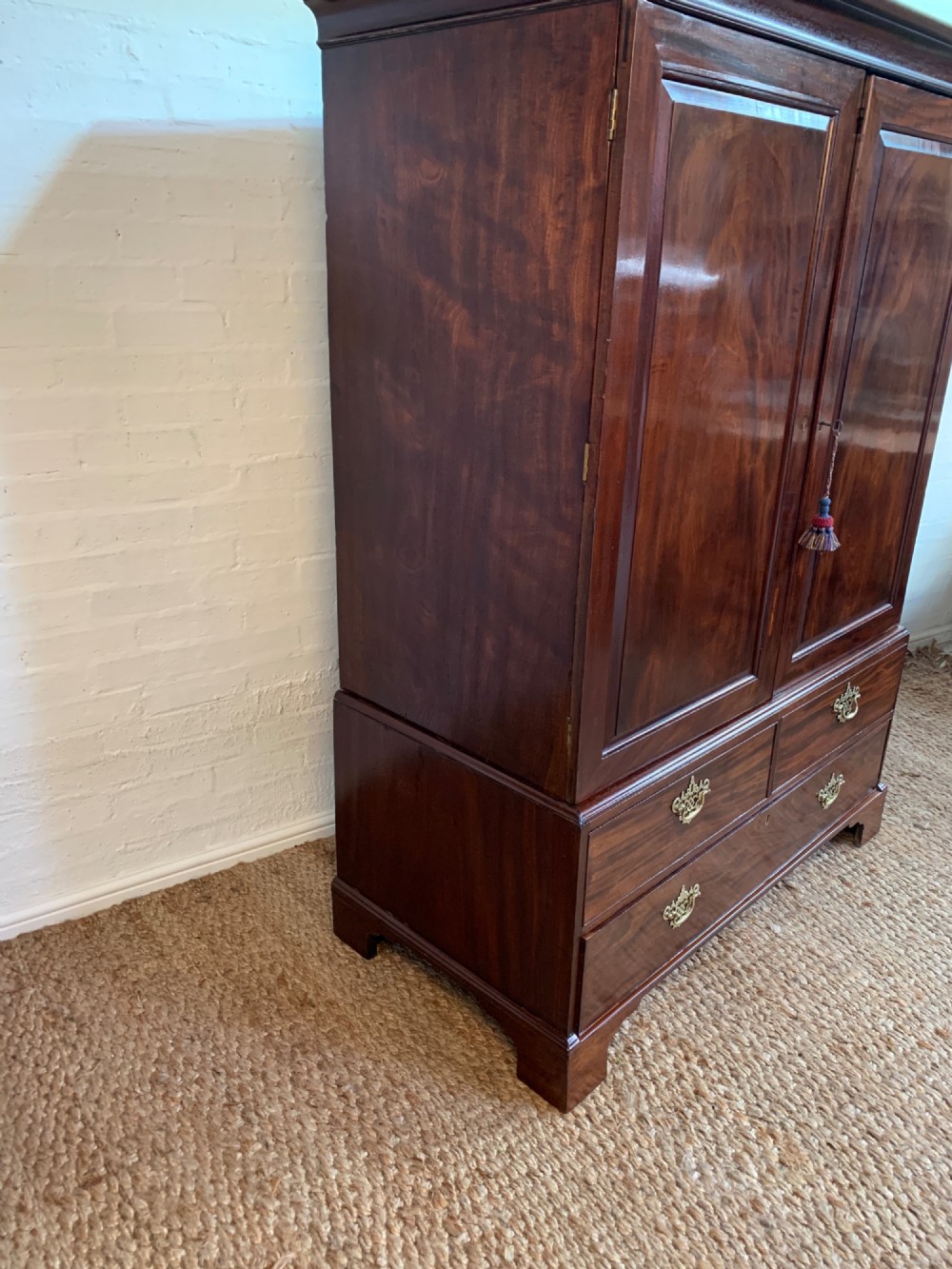 A 19th-century mahogany linen press featuring a two-door upper cupboard above a base with drawers and brass handles. View VI