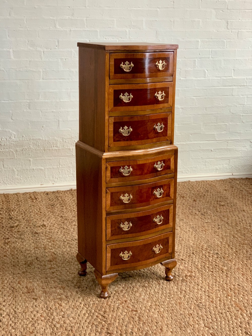 A narrow Queen Anne style walnut tallboy featuring seven drawers in a two-piece stacked design with brass handles and cabriole legs.
