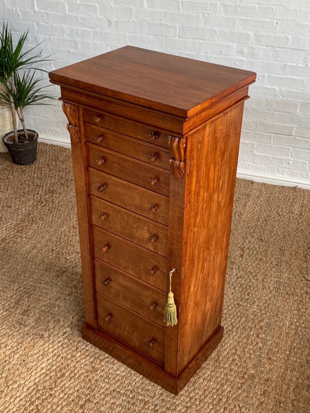 A tall Victorian figured mahogany Wellington chest with eight graduated drawers, turned wooden knobs, carved corbels, and a hinged side locking bar. View II