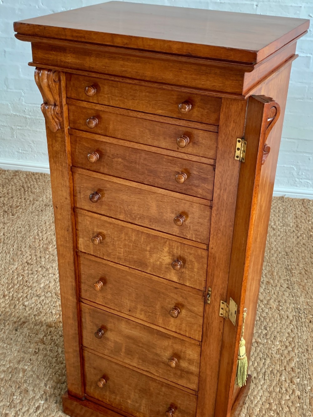 A tall Victorian figured mahogany Wellington chest with eight graduated drawers, turned wooden knobs, carved corbels, and a hinged side locking bar. View IV