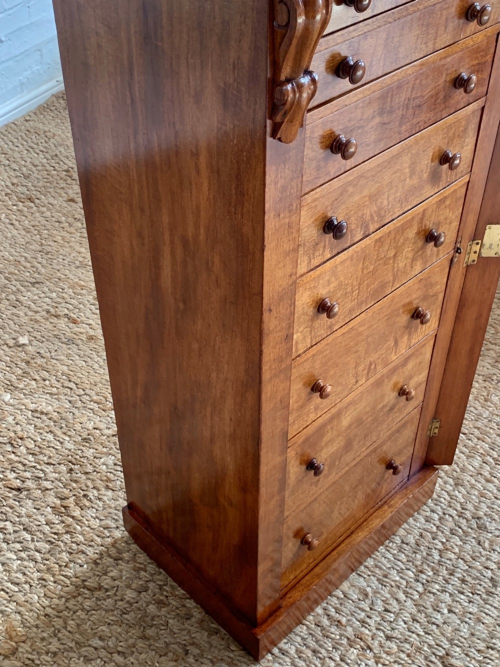 A tall Victorian figured mahogany Wellington chest with eight graduated drawers, turned wooden knobs, carved corbels, and a hinged side locking bar. View V