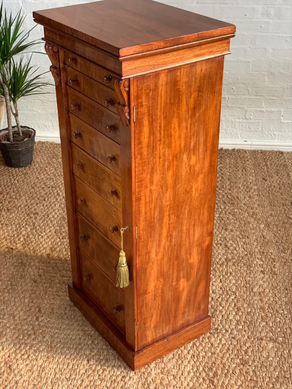 A tall Victorian figured mahogany Wellington chest with eight graduated drawers, turned wooden knobs, carved corbels, and a hinged side locking bar. View VI