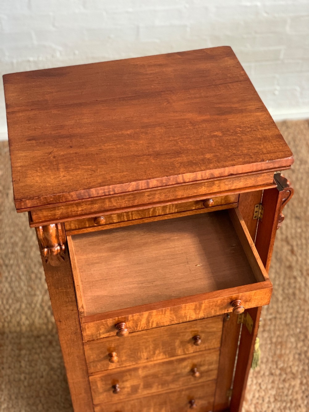 A tall Victorian figured mahogany Wellington chest with eight graduated drawers, turned wooden knobs, carved corbels, and a hinged side locking bar. View VIII