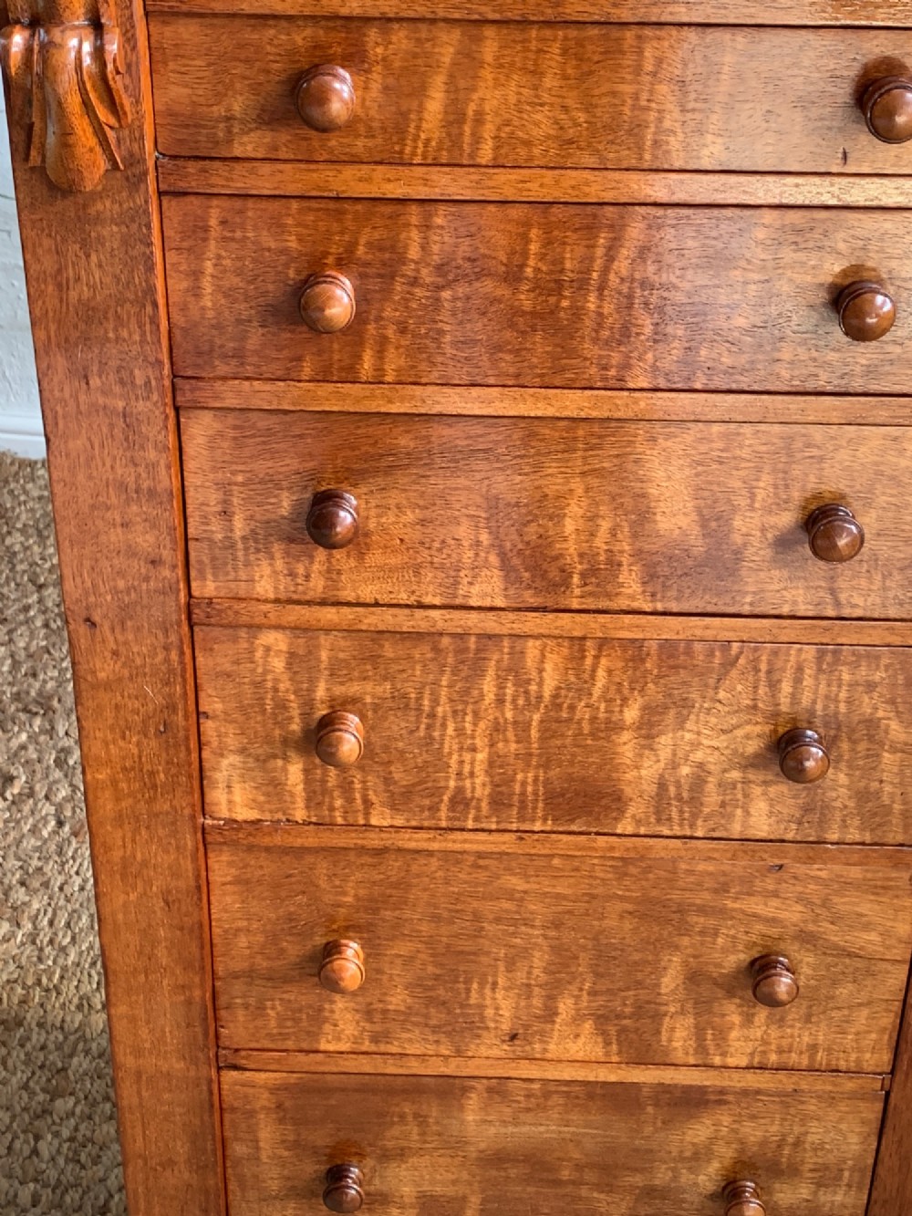 A tall Victorian figured mahogany Wellington chest with eight graduated drawers, turned wooden knobs, carved corbels, and a hinged side locking bar. View X
