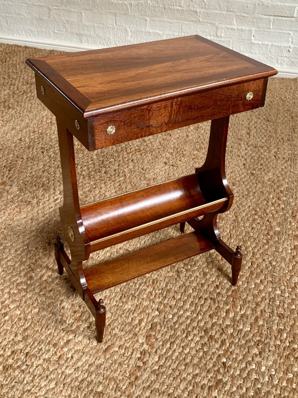 A dark mahogany Canterbury side table featuring a rectangular top, a single shallow drawer with brass knobs, and a lower V-shaped magazine trough supported on shaped uprights.