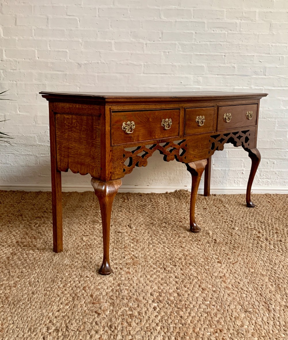 An Edwardian oak dresser base featuring three drawers with brass handles, a decorative pierced fretwork apron, and four cabriole legs terminating in pad feet.