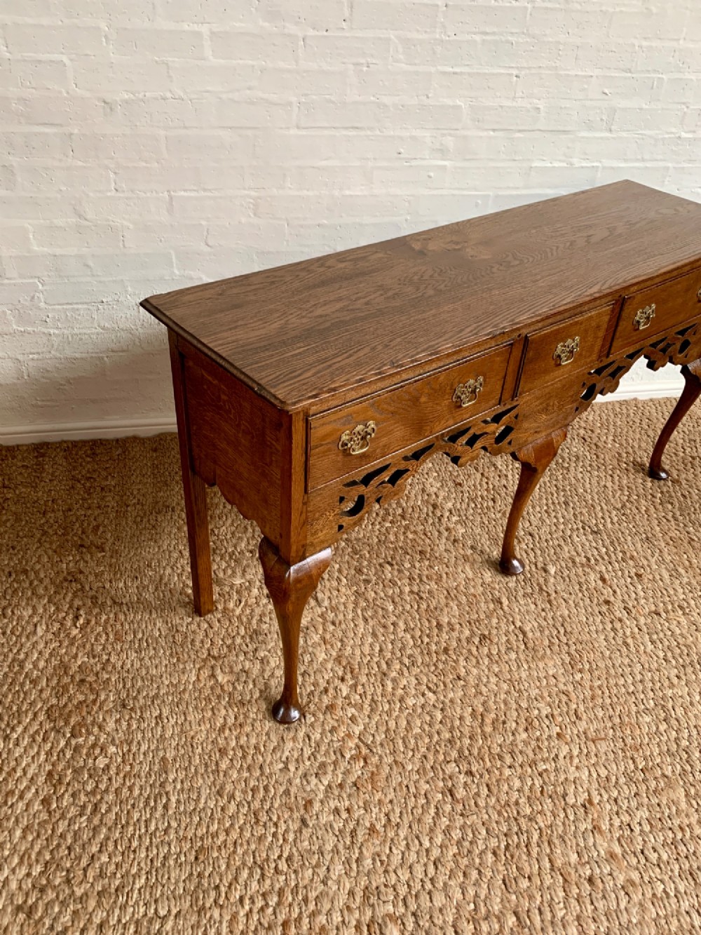 An Edwardian oak dresser base featuring three drawers with brass handles, a decorative pierced fretwork apron, and four cabriole legs terminating in pad feet. View II