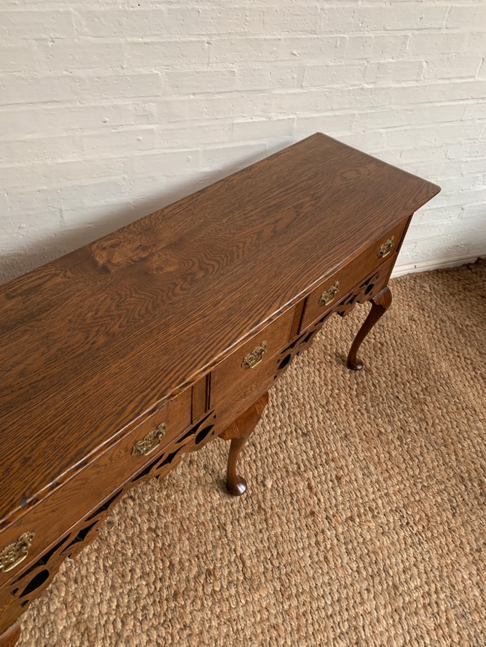 An Edwardian oak dresser base featuring three drawers with brass handles, a decorative pierced fretwork apron, and four cabriole legs terminating in pad feet. View III