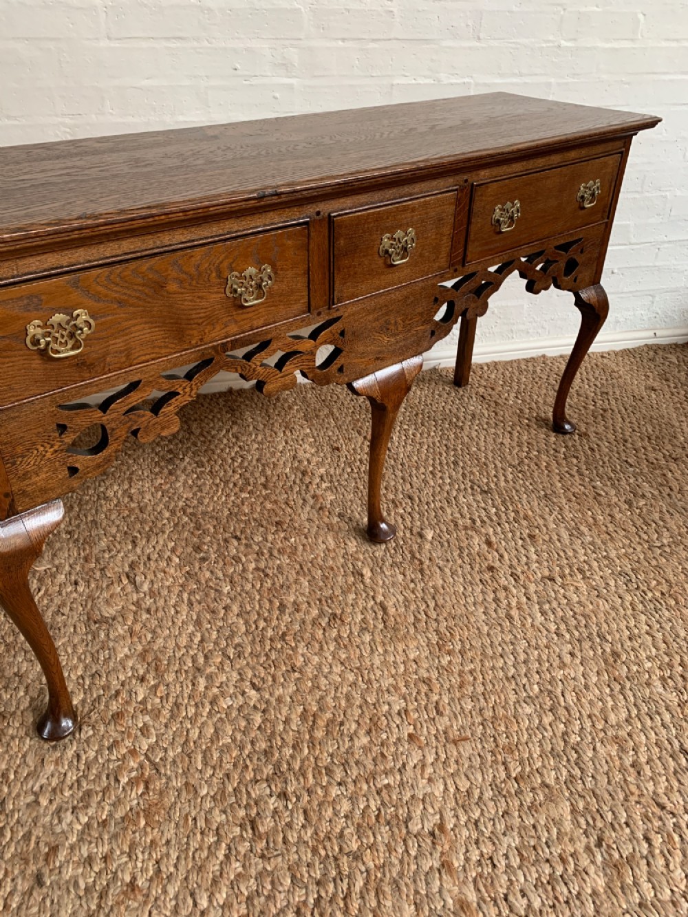 An Edwardian oak dresser base featuring three drawers with brass handles, a decorative pierced fretwork apron, and four cabriole legs terminating in pad feet. View VI