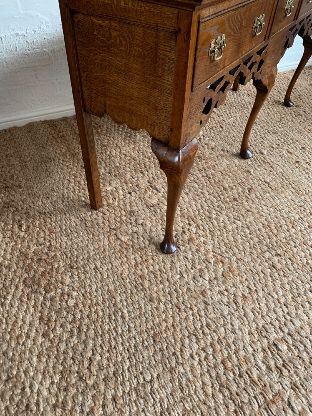 An Edwardian oak dresser base featuring three drawers with brass handles, a decorative pierced fretwork apron, and four cabriole legs terminating in pad feet. View IX