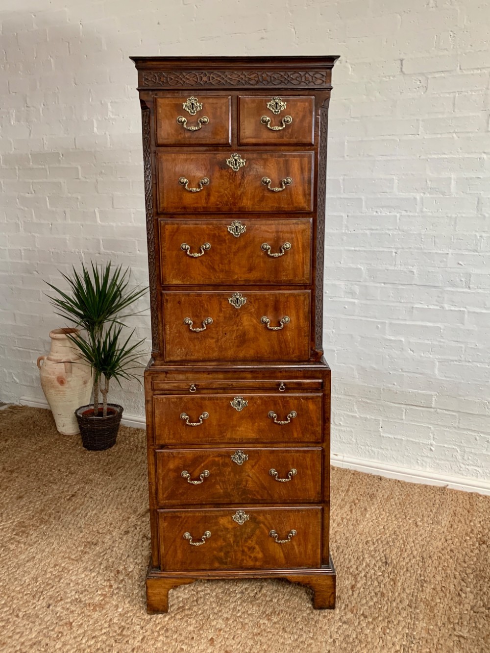 A tall 19th-century George III style burr walnut chest of drawers featuring decorative brass handles, keyhole escutcheons, carved side friezes, and bracket feet.