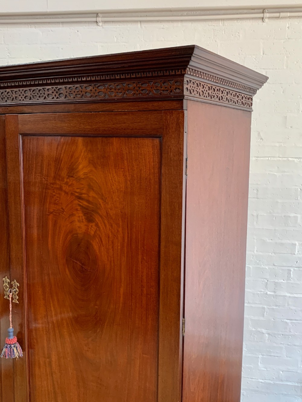 A nineteenth-century dark mahogany linen press featuring a carved blind fretwork cornice, twin flame-mahogany cupboard doors, and four lower drawers with brass drop handles. View II