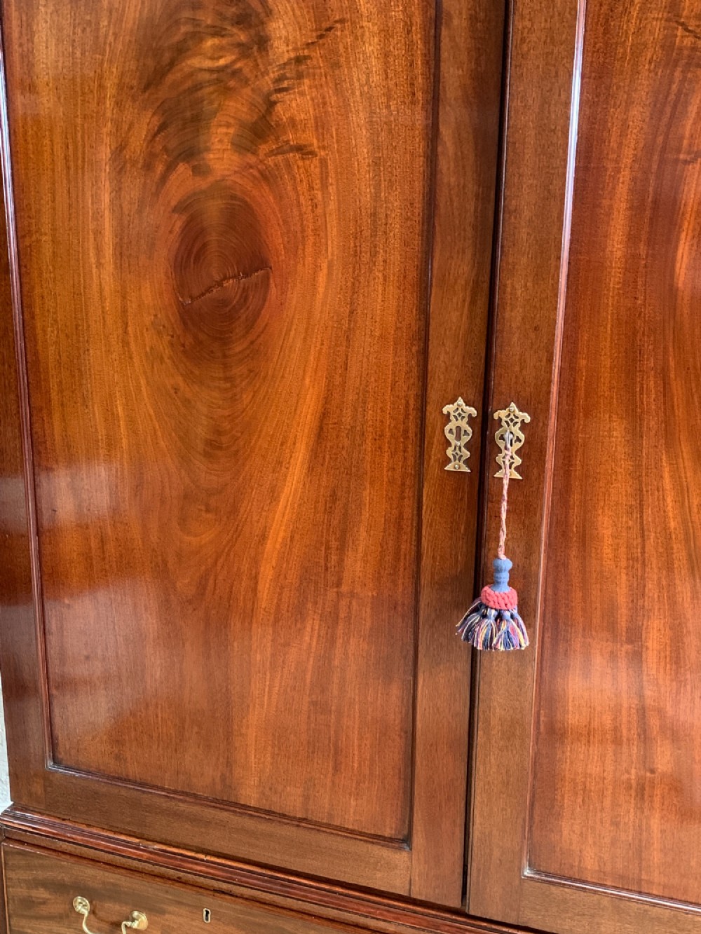 A nineteenth-century dark mahogany linen press featuring a carved blind fretwork cornice, twin flame-mahogany cupboard doors, and four lower drawers with brass drop handles. View III