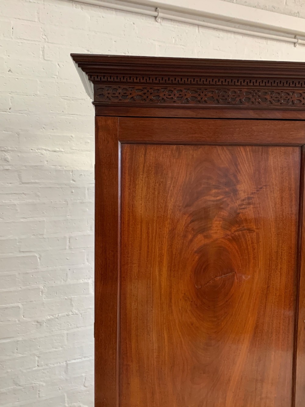 A nineteenth-century dark mahogany linen press featuring a carved blind fretwork cornice, twin flame-mahogany cupboard doors, and four lower drawers with brass drop handles. View IV