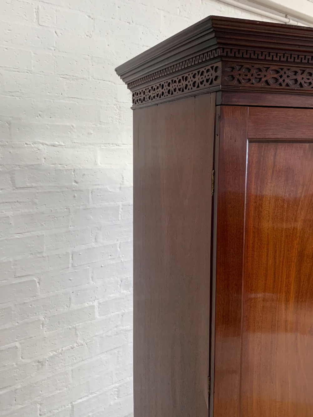 A nineteenth-century dark mahogany linen press featuring a carved blind fretwork cornice, twin flame-mahogany cupboard doors, and four lower drawers with brass drop handles. View V