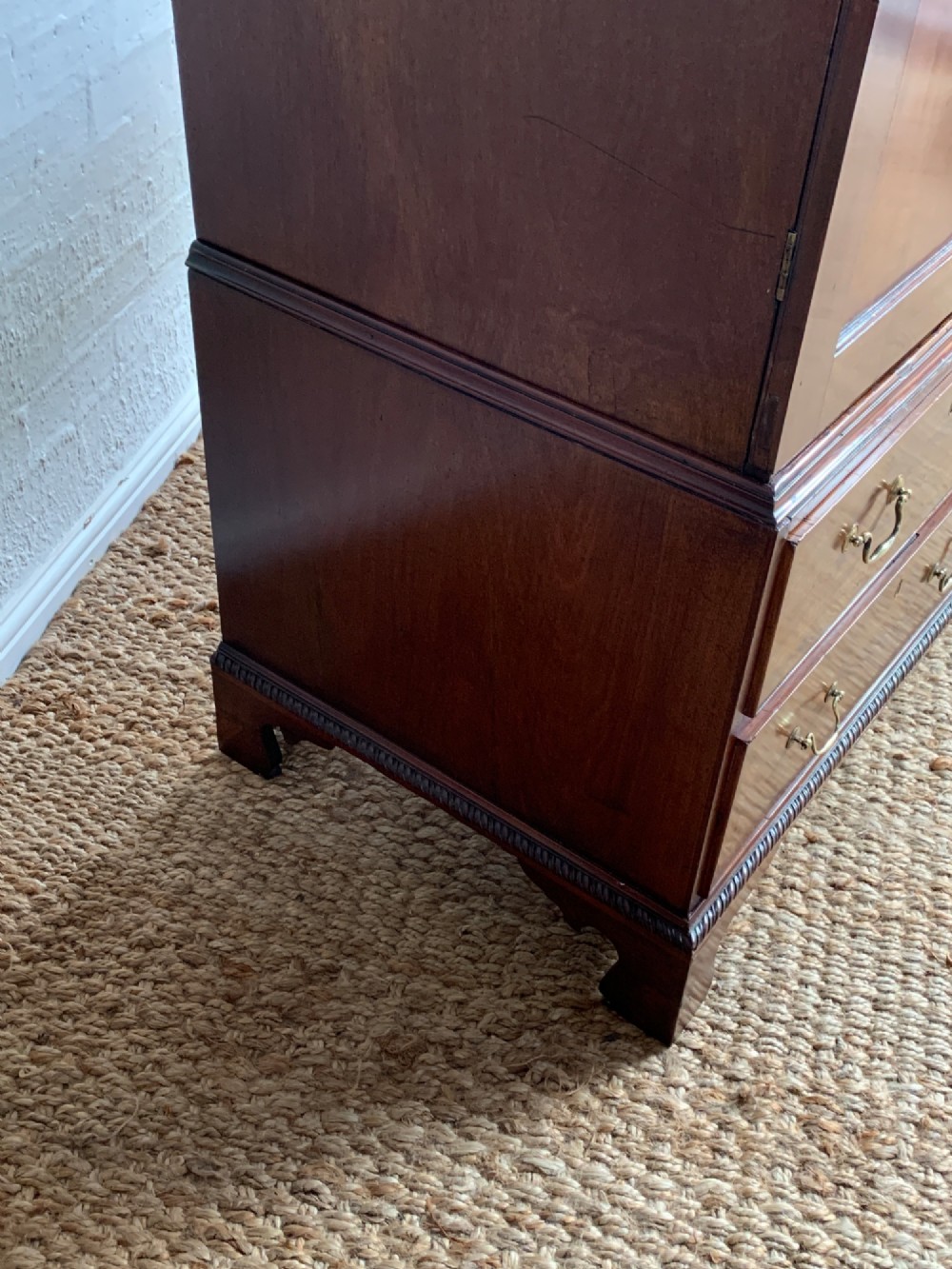 A nineteenth-century dark mahogany linen press featuring a carved blind fretwork cornice, twin flame-mahogany cupboard doors, and four lower drawers with brass drop handles. View VI