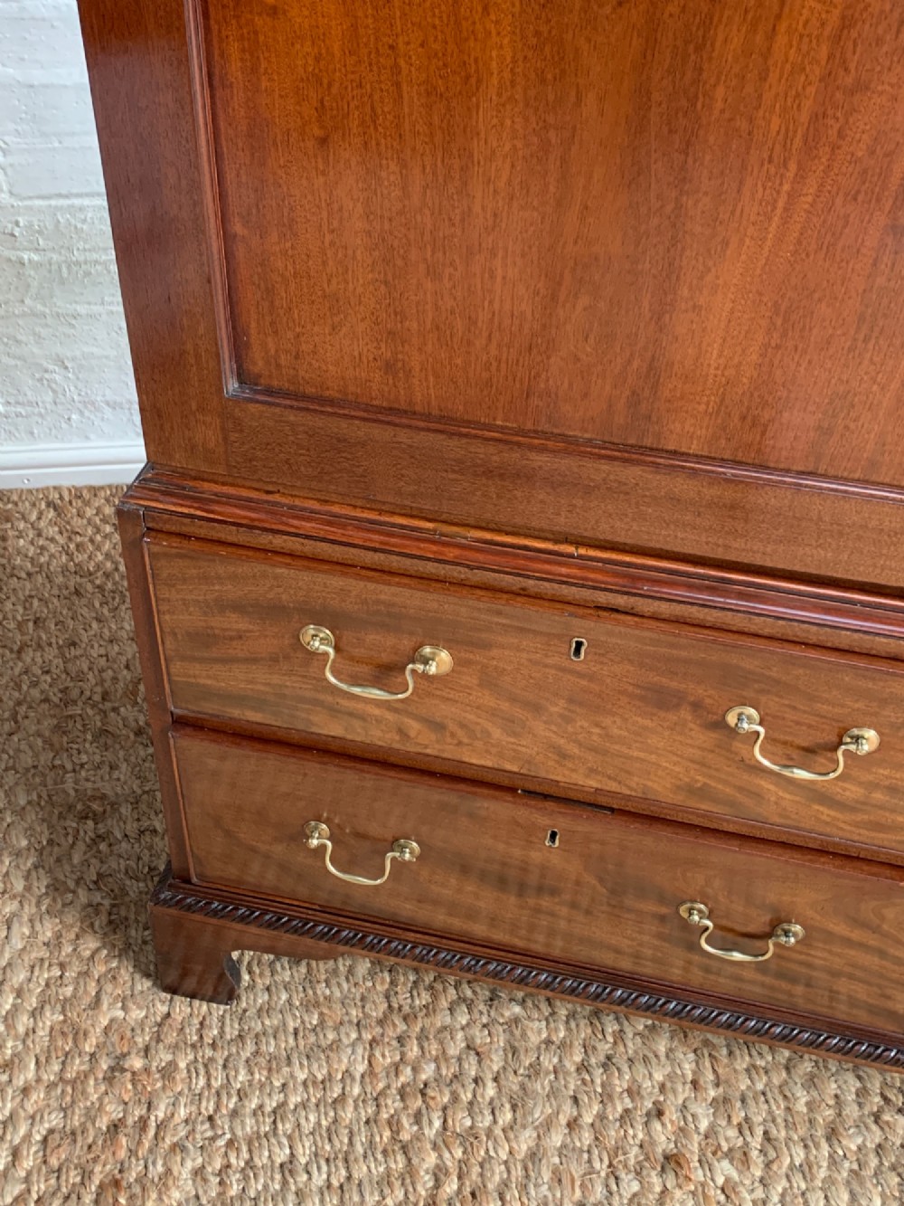 A nineteenth-century dark mahogany linen press featuring a carved blind fretwork cornice, twin flame-mahogany cupboard doors, and four lower drawers with brass drop handles. View VII
