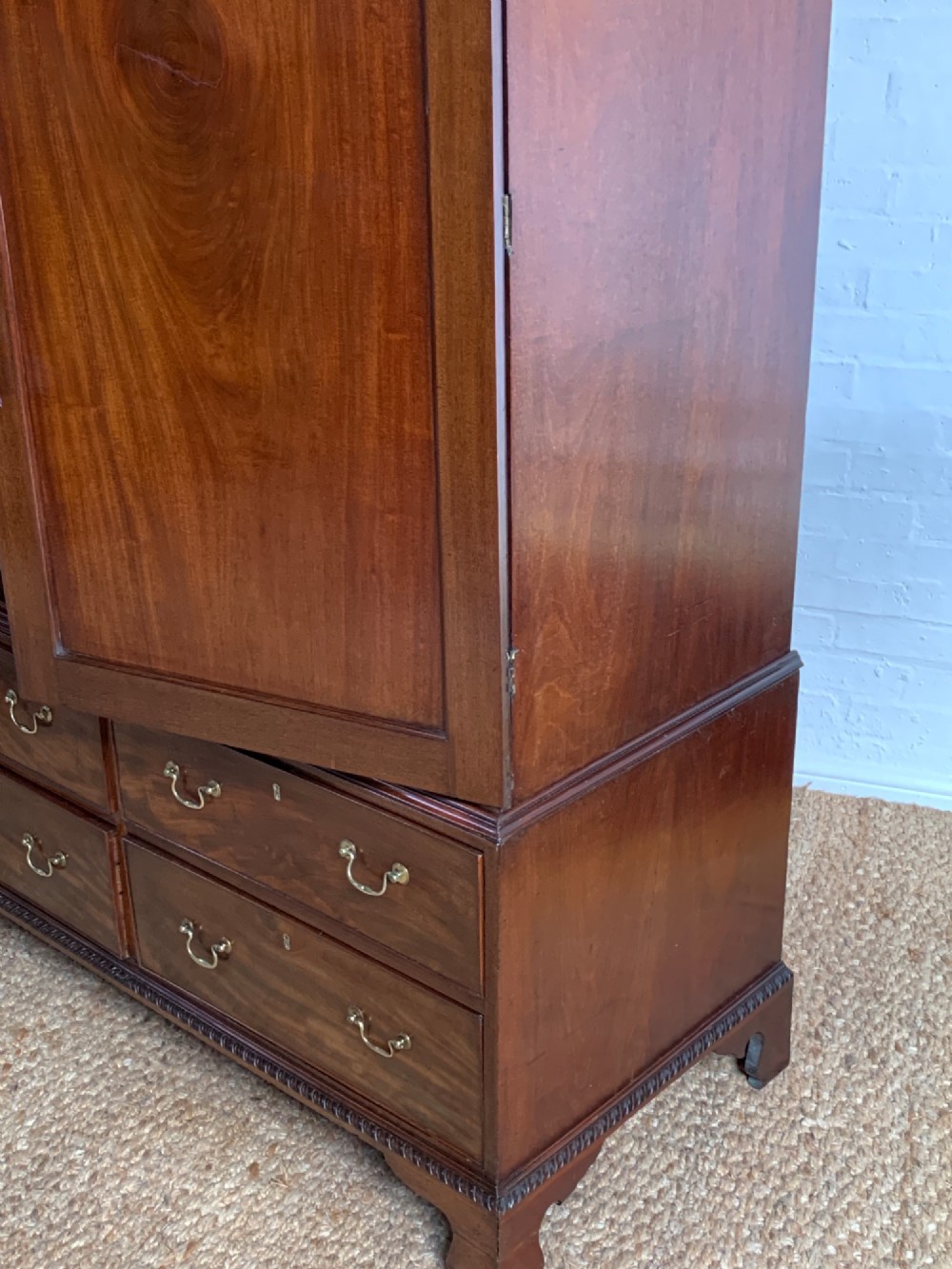 A nineteenth-century dark mahogany linen press featuring a carved blind fretwork cornice, twin flame-mahogany cupboard doors, and four lower drawers with brass drop handles. View VIII