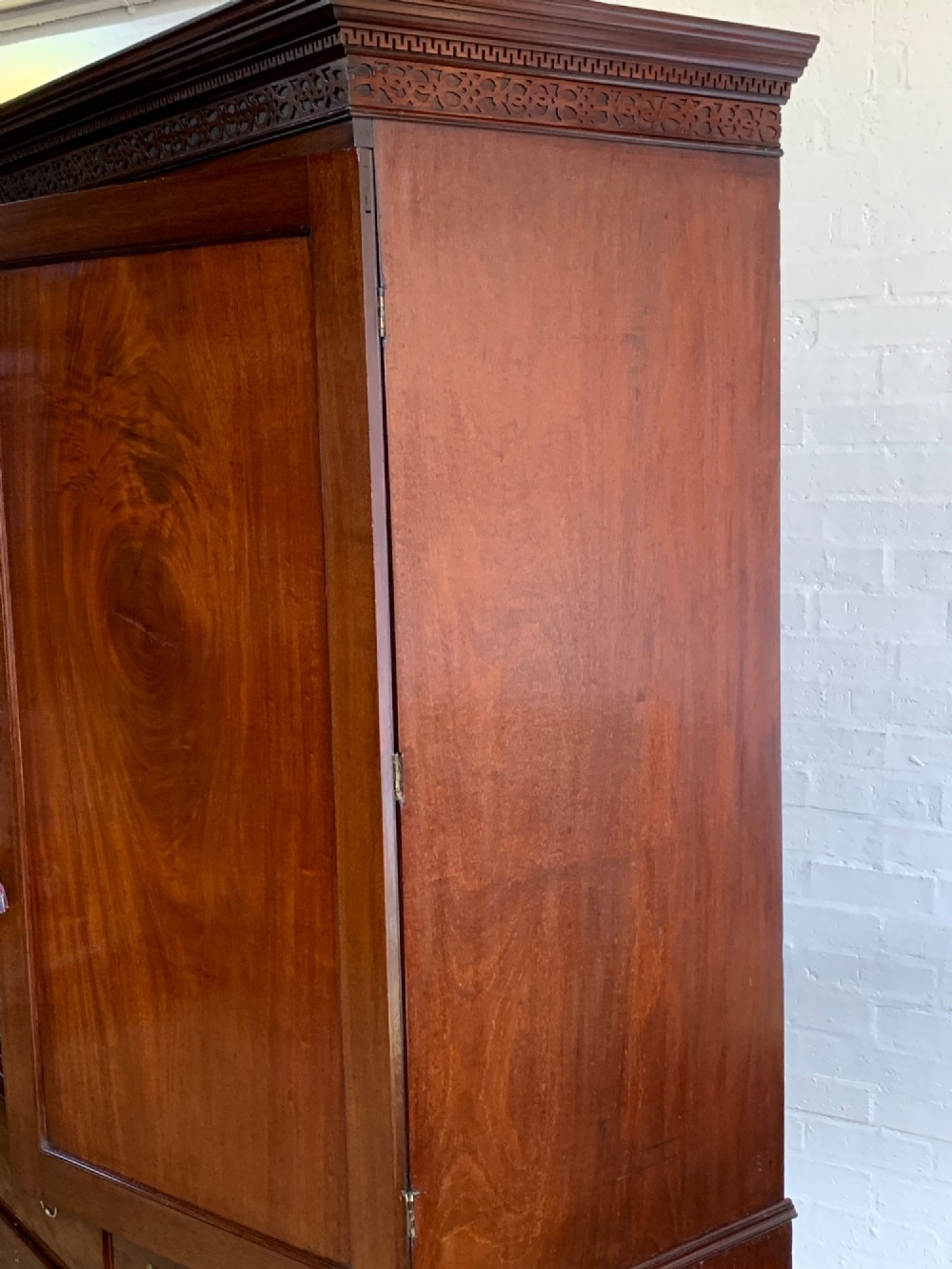 A nineteenth-century dark mahogany linen press featuring a carved blind fretwork cornice, twin flame-mahogany cupboard doors, and four lower drawers with brass drop handles. View IX