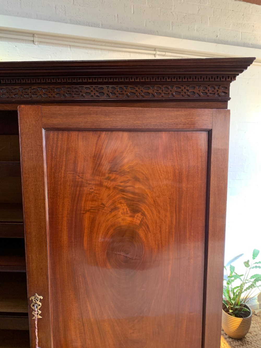 A nineteenth-century dark mahogany linen press featuring a carved blind fretwork cornice, twin flame-mahogany cupboard doors, and four lower drawers with brass drop handles. View X