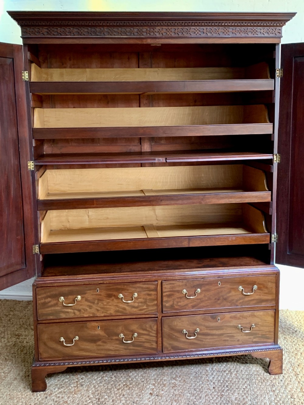 A nineteenth-century dark mahogany linen press featuring a carved blind fretwork cornice, twin flame-mahogany cupboard doors, and four lower drawers with brass drop handles. View XI