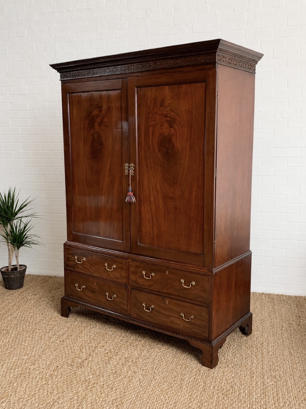 A nineteenth-century dark mahogany linen press featuring a carved blind fretwork cornice, twin flame-mahogany cupboard doors, and four lower drawers with brass drop handles.