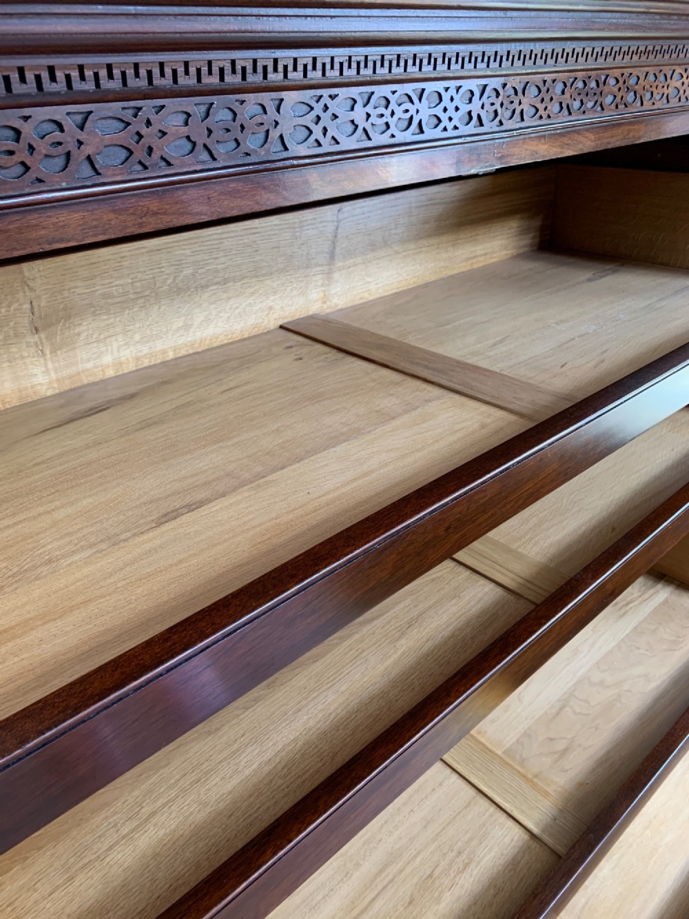 A nineteenth-century dark mahogany linen press featuring a carved blind fretwork cornice, twin flame-mahogany cupboard doors, and four lower drawers with brass drop handles. View XII
