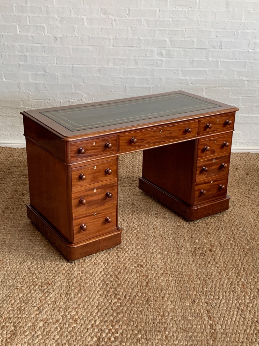 Victorian mahogany pedestal desk featuring an olive green gold-tooled leather inset top and nine drawers with turned wooden knobs.