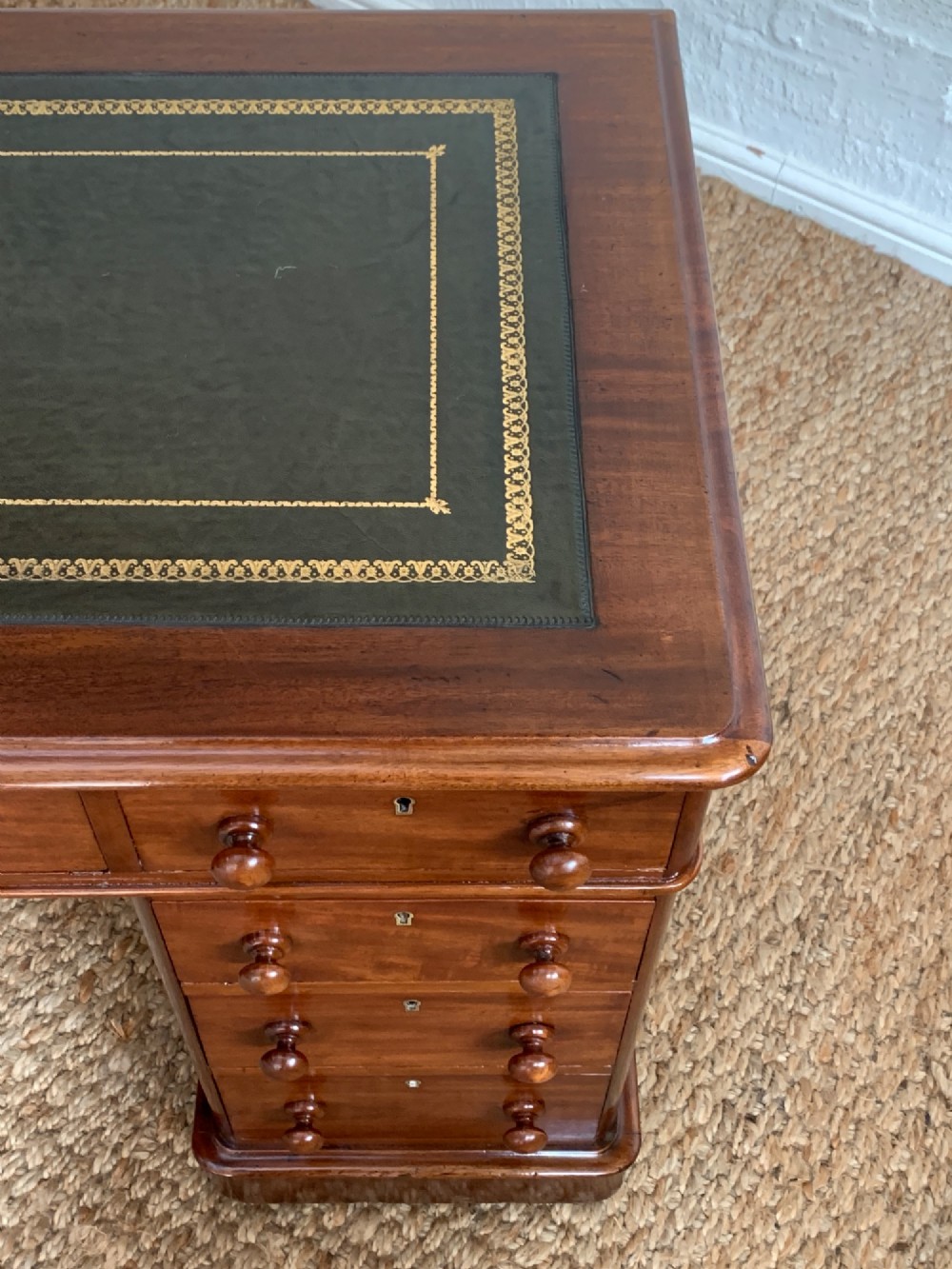 Victorian mahogany pedestal desk featuring an olive green gold-tooled leather inset top and nine drawers with turned wooden knobs. View IV