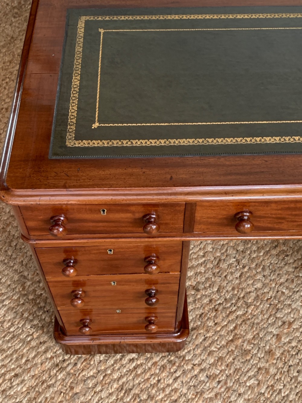 Victorian mahogany pedestal desk featuring an olive green gold-tooled leather inset top and nine drawers with turned wooden knobs. View V