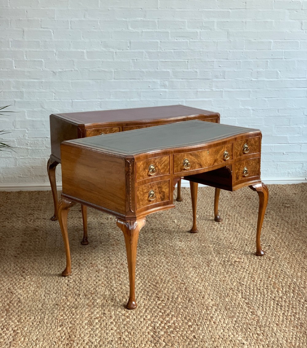 An early 20th-century burr walnut writing desk featuring an inset leather top, kneehole drawer arrangement, brass drop handles, and cabriole legs.