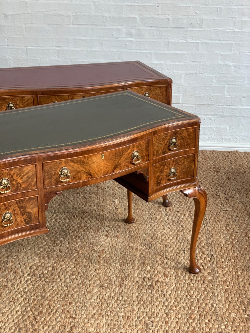 An early 20th-century burr walnut writing desk featuring an inset leather top, kneehole drawer arrangement, brass drop handles, and cabriole legs. View II
