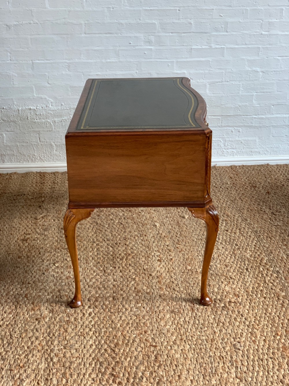 An early 20th-century burr walnut writing desk featuring an inset leather top, kneehole drawer arrangement, brass drop handles, and cabriole legs. View III
