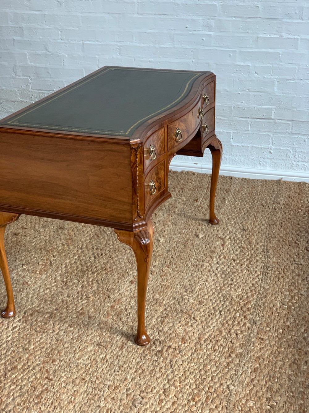 An early 20th-century burr walnut writing desk featuring an inset leather top, kneehole drawer arrangement, brass drop handles, and cabriole legs. View V