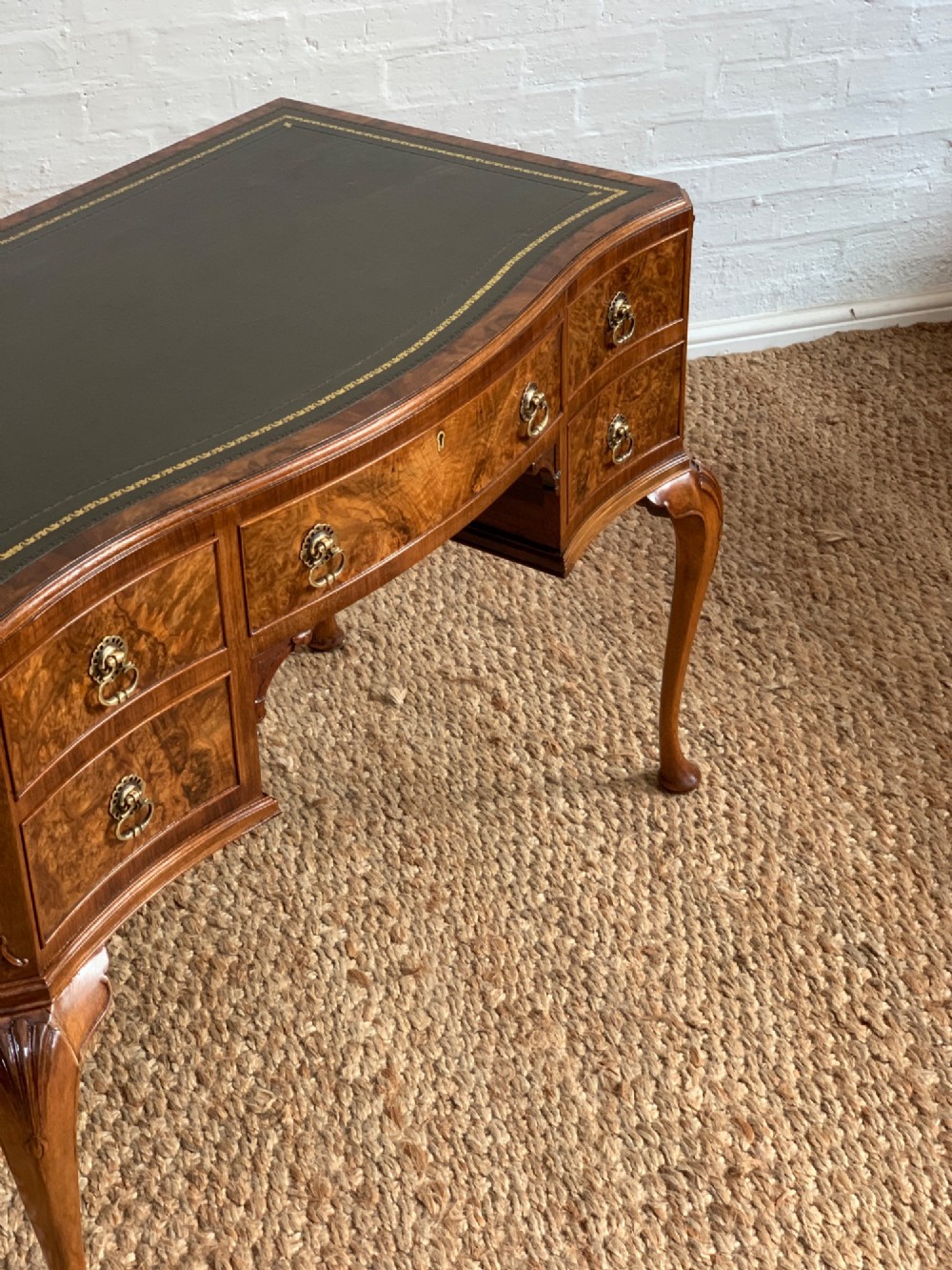 An early 20th-century burr walnut writing desk featuring an inset leather top, kneehole drawer arrangement, brass drop handles, and cabriole legs. View VIII