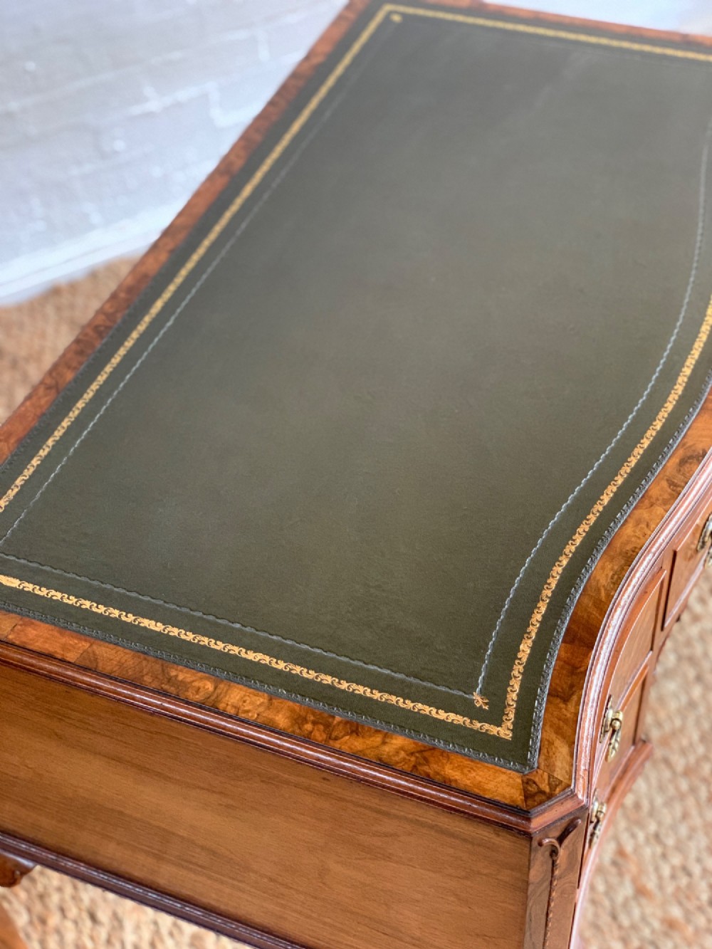 An early 20th-century burr walnut writing desk featuring an inset leather top, kneehole drawer arrangement, brass drop handles, and cabriole legs. View IX