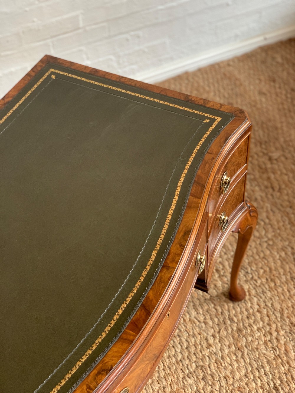 An early 20th-century burr walnut writing desk featuring an inset leather top, kneehole drawer arrangement, brass drop handles, and cabriole legs. View X