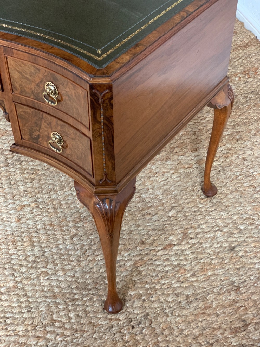 An early 20th-century burr walnut writing desk featuring an inset leather top, kneehole drawer arrangement, brass drop handles, and cabriole legs. View XI