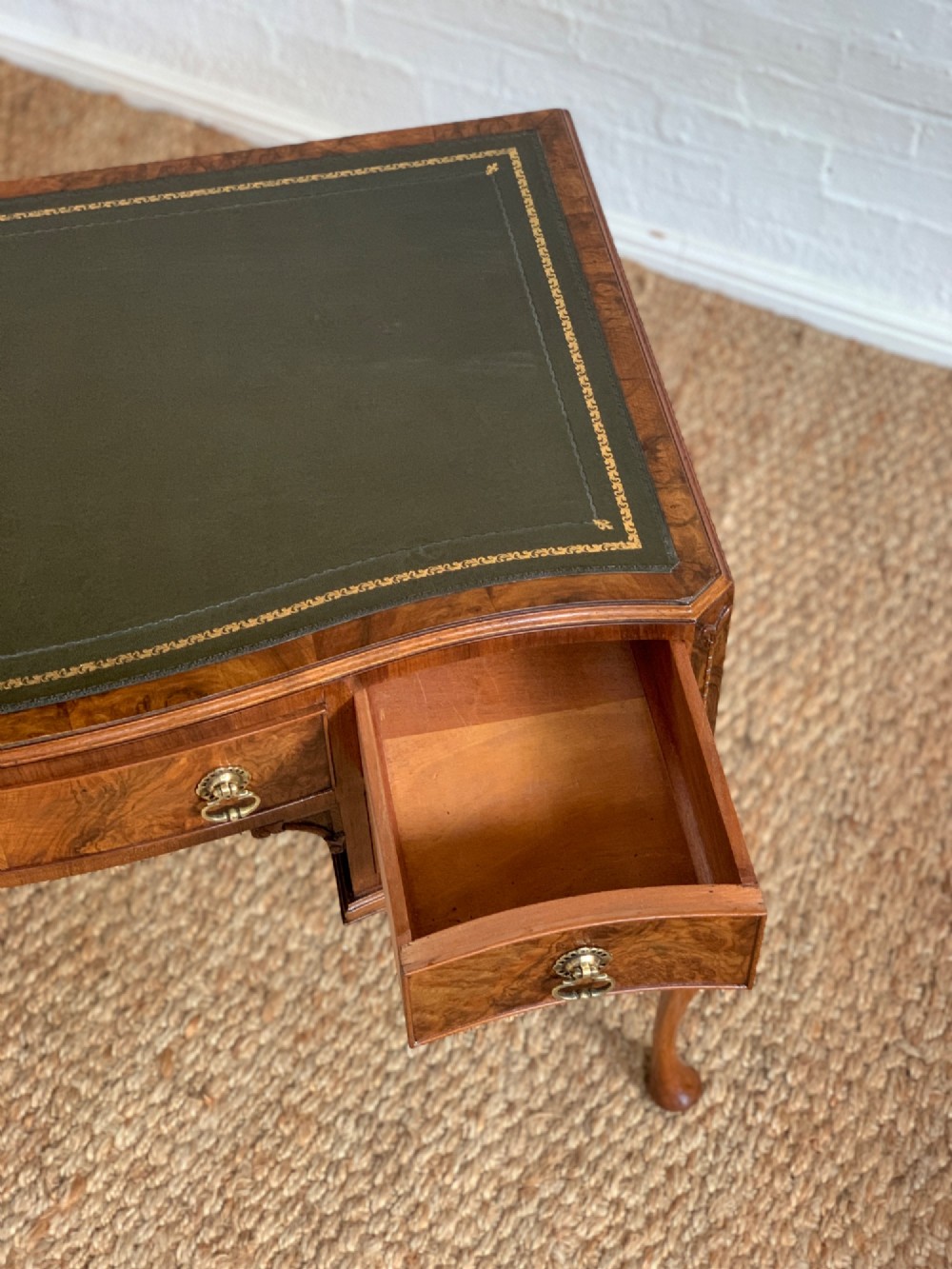 An early 20th-century burr walnut writing desk featuring an inset leather top, kneehole drawer arrangement, brass drop handles, and cabriole legs. View XII