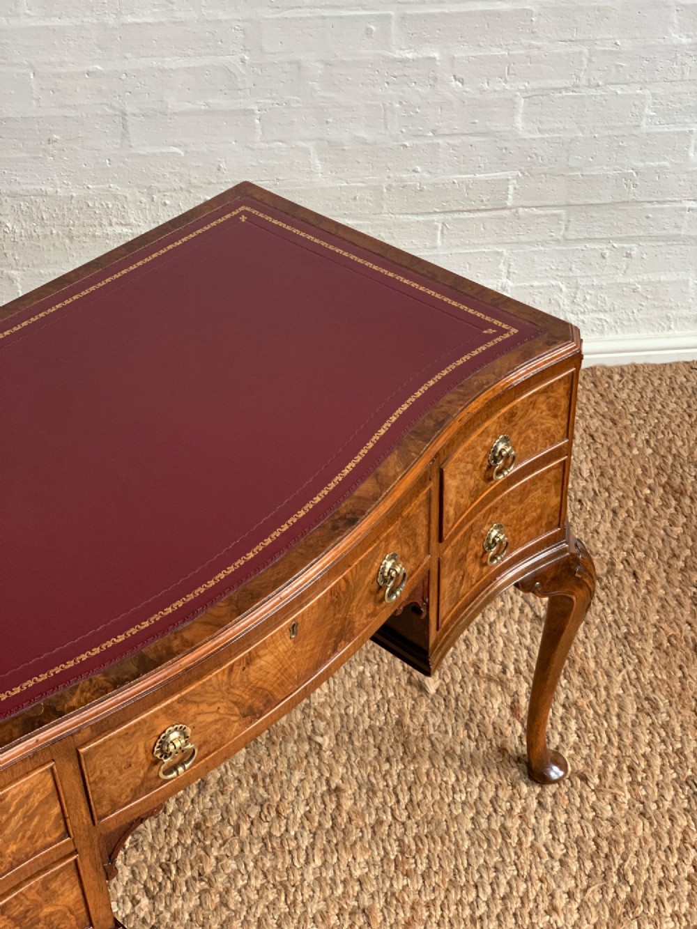 An early 20th-century burr walnut writing desk featuring five drawers with brass handles, carved cabriole legs, and a fitted kneehole. View III