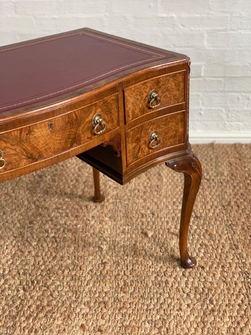 An early 20th-century burr walnut writing desk featuring five drawers with brass handles, carved cabriole legs, and a fitted kneehole. View IV